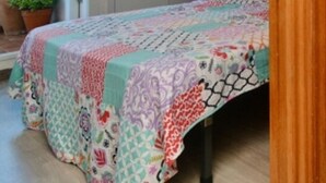 Ein Zimmer mit einem Bett, das mit einem farbenfrohen Patchwork-Quilt bezogen ist, einem Holzschrank und einem weißen Hocker.