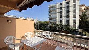 Een balkon met een tafel en vier stoelen, met uitzicht op een woonwijk met gebouwen en bomen.