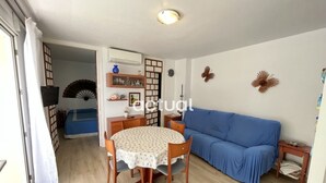 A living room with a blue sofa, a dining table with chairs, and a TV mounted on the wall. - Seaside apartment with terrace, optional AC, parking, and WIFI (Platja d'Aro)