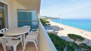 A balcony with a table and chairs, overlooking a beach with a clear view of the sea and distant buildings. - 2-bedroom apartment with terrace, sea view and parking in Platja d'Aro (Platja d'Aro)