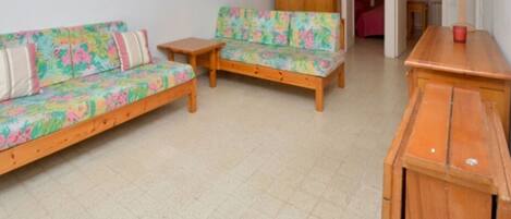 Een kamer met twee houten banken met bloemrijk gestoffeerde bekleding, een klein houten tafeltje en een houten kast.
