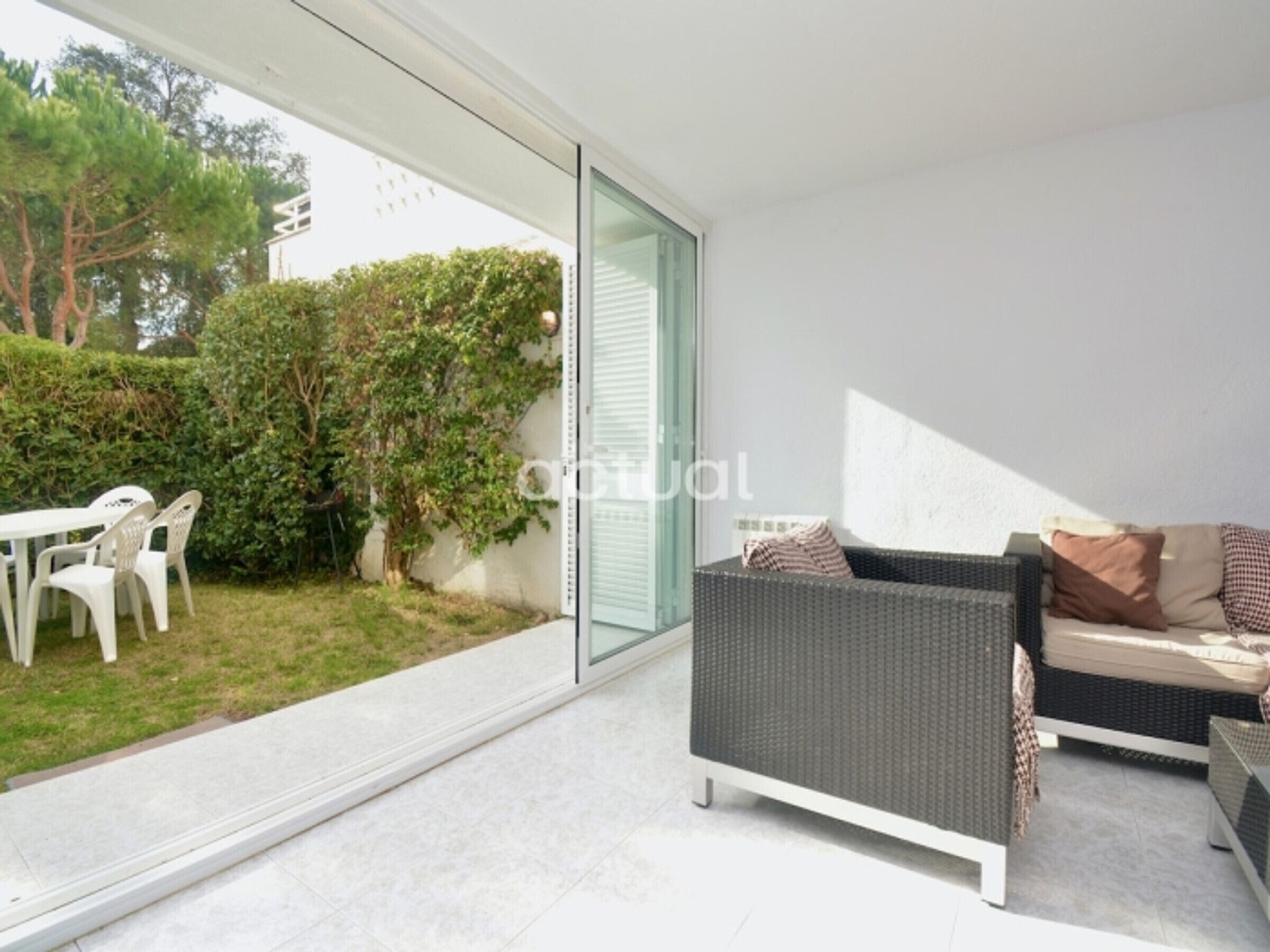 Un salon moderne doté d’une porte coulissante en verre donnant sur un jardin, d’un canapé en osier et d’une petite table avec des chaises.