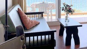 A room with a white sofa, a small table with a vase, and a view of the sea through a glass door. - Beachfront apartment: 1 bedroom, terrace, parking (Platja d'Aro)