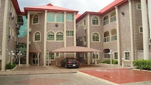 A large building with multiple floors, arched windows, and a red roof. There is a car parked in front and a covered area with a canopy. - Bovina View Hotel (Ilorin)