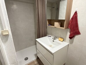 Un baño con ducha, lavamanos con espejo y toallero.