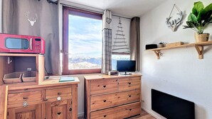 A compact room with a wooden desk, a television, a microwave, and a window with a mountain view. - Ski-in/Ski-out Studio, 2 guests, Le Corbier Residence (Le Corbier)