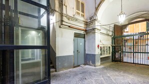 Un couloir intérieur doté d’un sol en pierre, d’une grille métallique et d’une porte bleue.