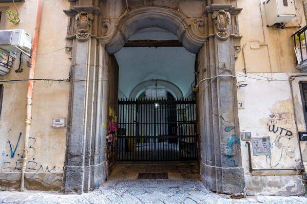 An arched entrance with a metal gate, a stone wall with graffiti, and a utility box.