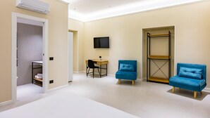 Une chambre moderne équipée d’un bureau, de deux chaises bleues, d’un téléviseur et d’une étagère.