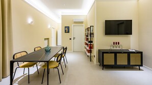 Un espace repas comprenant une longue table, des chaises, un téléviseur et une bibliothèque.