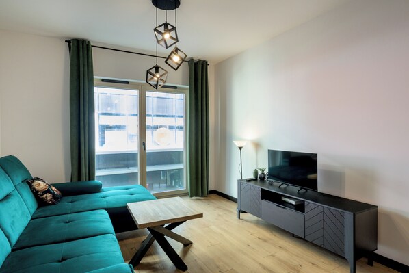 A modern living room with a teal sofa, wooden coffee table, and a TV on a grey cabinet. - RentPlanet - Apartament Czysta (Wroclaw)