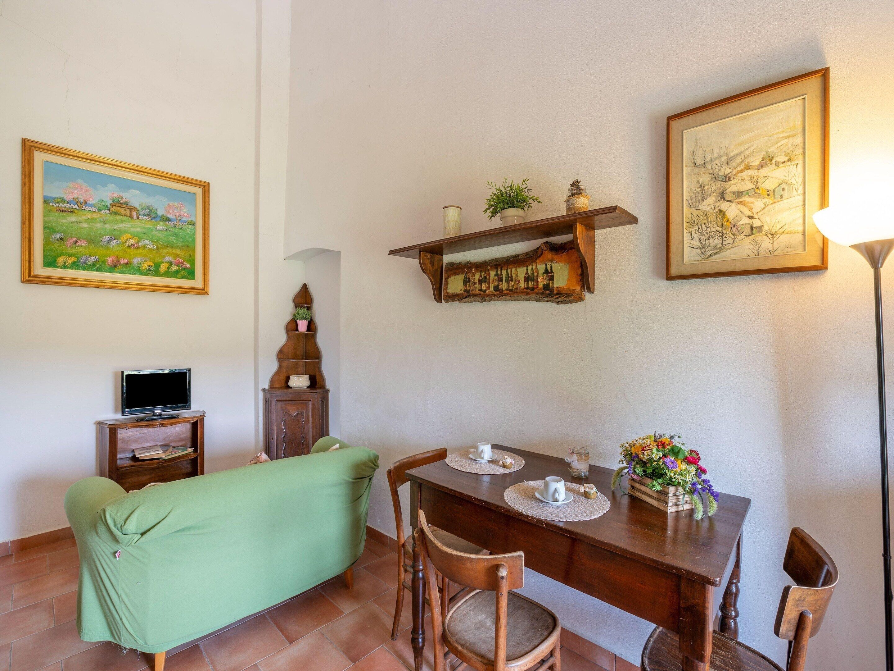 A dining area with a wooden table, chairs, a green sofa, a TV, and wall-mounted shelves with decorative items.