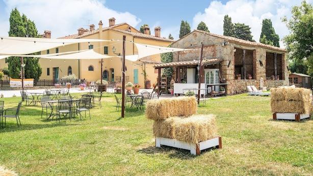 An outdoor seating area with tables and chairs, hay bales, and a building with a stone facade. - Apartment in Tuscany Near Pisa and Beaches (Collesalvetti)