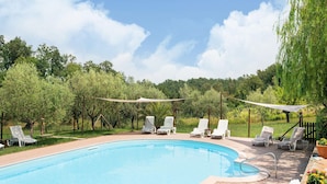 A swimming pool with lounge chairs and a shaded area, surrounded by trees and greenery. - Apartment in Tuscany Near Pisa and Beaches (Collesalvetti)