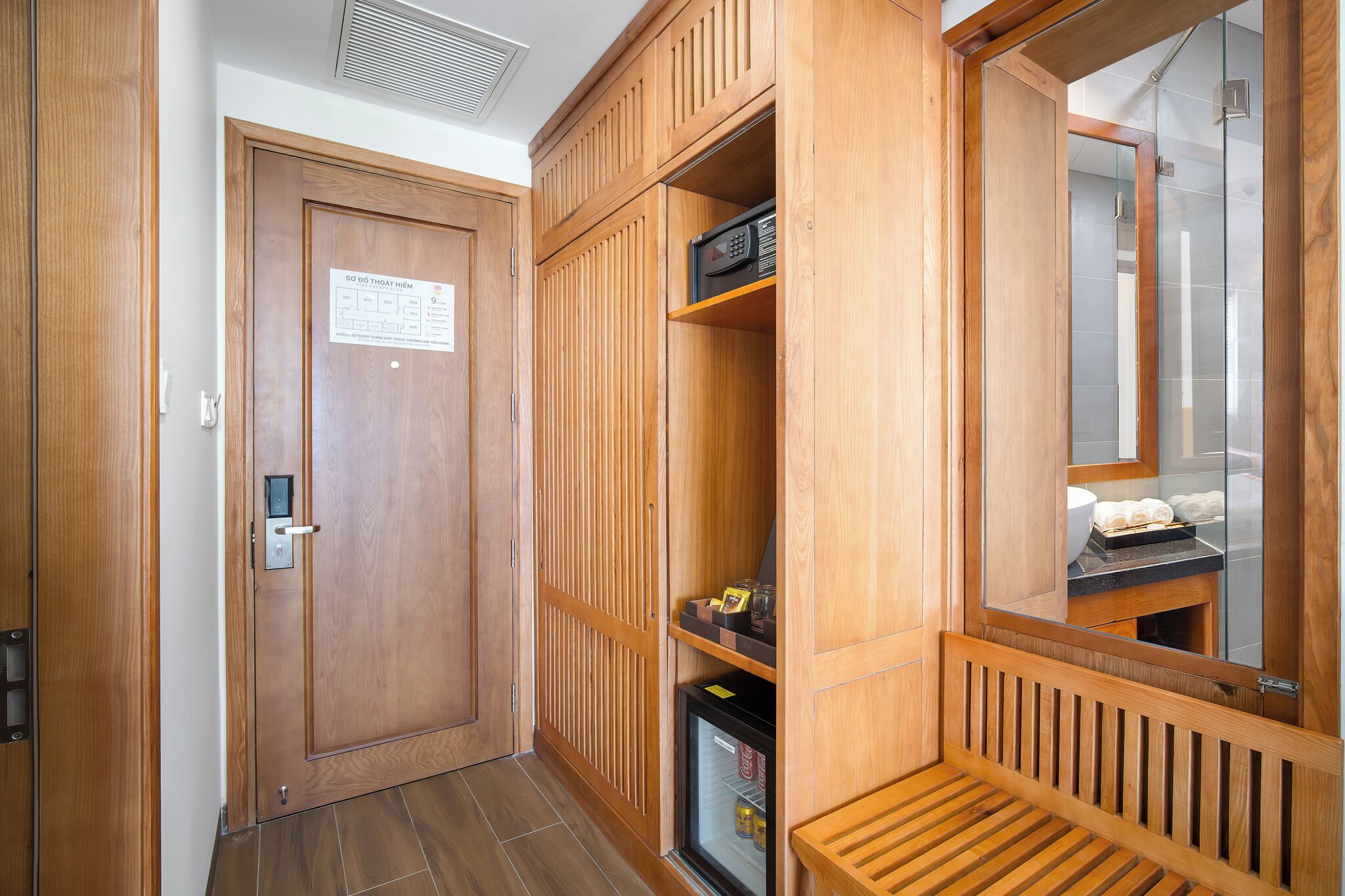A wooden wardrobe with a mirror, a microwave, and a small shelf with toiletries.