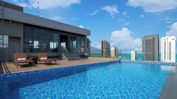 Un edificio moderno con piscina, zona de estar exterior y vistas al océano y al horizonte de la ciudad.