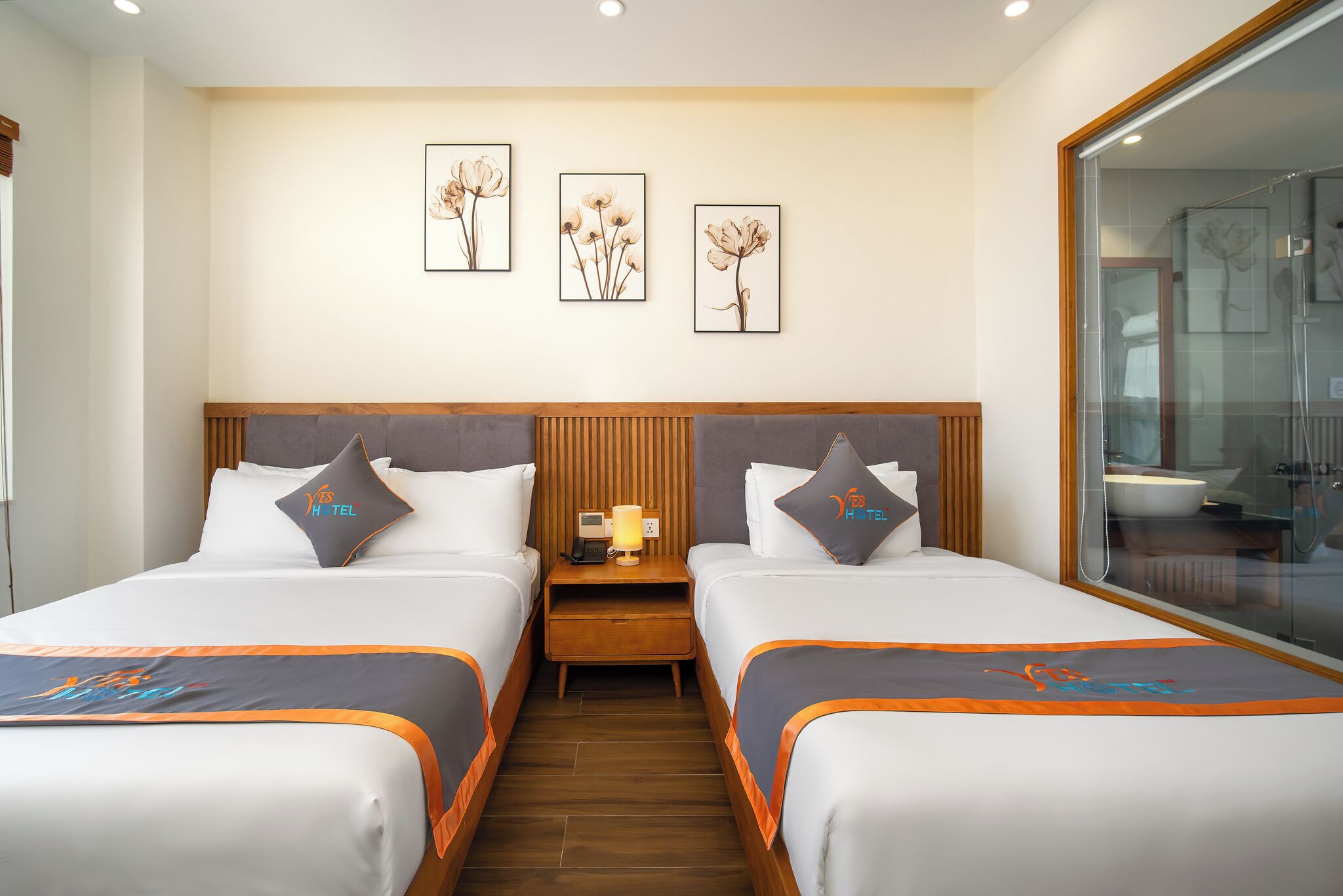 Una habitación de hotel con dos camas, un cabecero de madera, una mesita de noche con una lámpara y cuadros enmarcados en la pared.