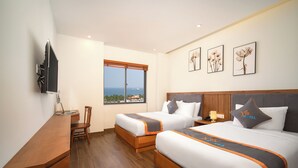 Habitación de hotel con dos camas, un escritorio, una silla y un televisor. Hay cuadros en la pared y una ventana con vistas.