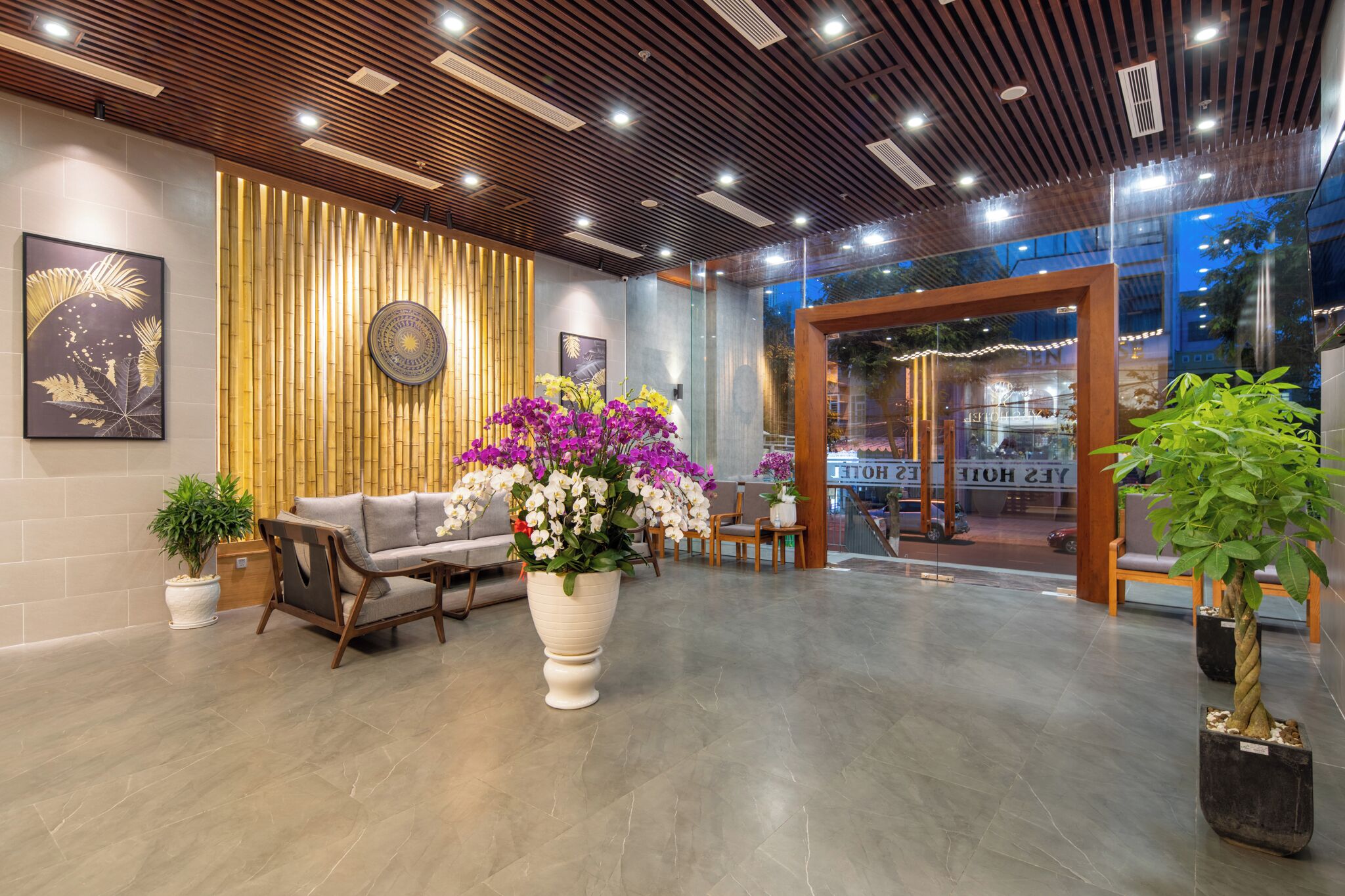 Eine moderne Lobby mit Holzboden, einer Rezeption, einer Sitzecke und Topfpflanzen.