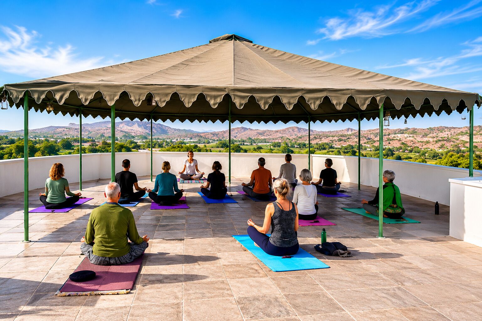 A group of people meditating on yoga mats under a canopy on a rooftop with a scenic view.