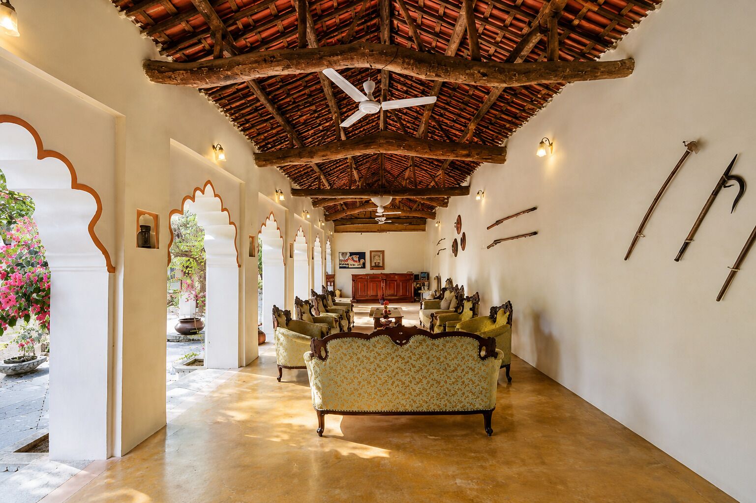 A spacious lobby with a high ceiling, traditional wooden beams, and a ceiling fan. There are several ornate chairs and a sofa arranged for seating.