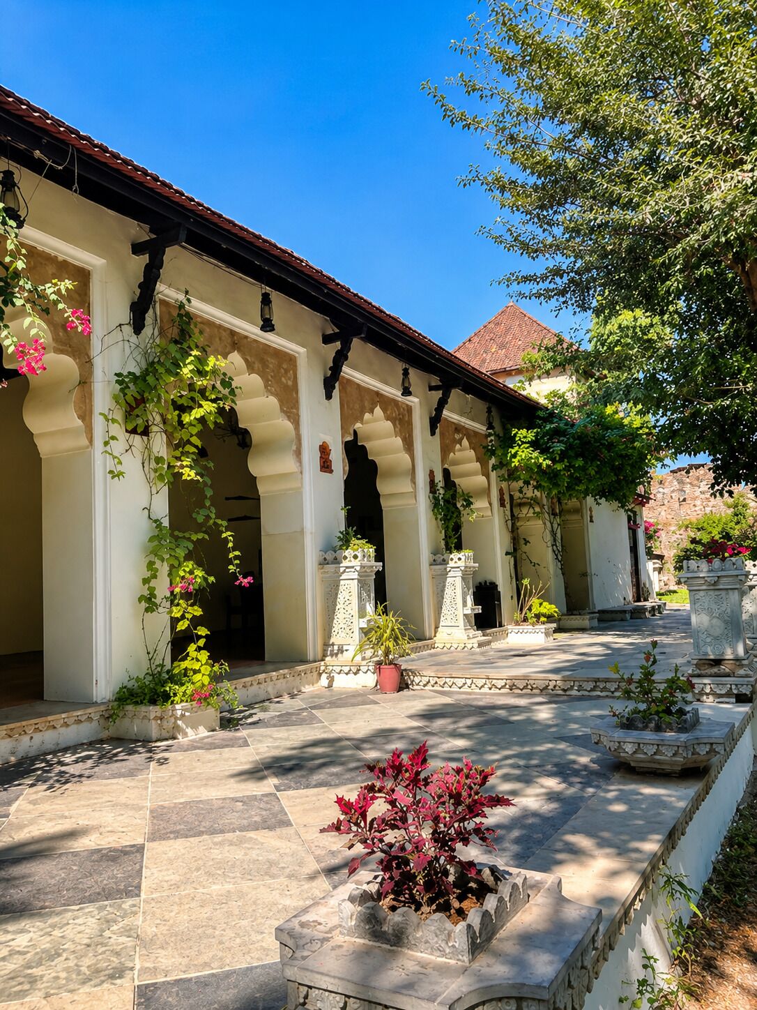Un patio con piso de baldosas, columnas blancas y plantas en macetas.