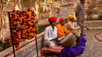 Un muro de piedra con una barandilla metálica decorativa, un grupo de personas tocando instrumentos musicales tradicionales, y un hombre tocando una flauta.