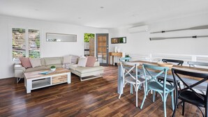 Un salon moderne avec un plancher en bois, des meubles blancs et un coin repas comprenant une table et des chaises en bois.