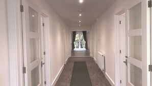 A long, narrow hallway with white doors on both sides, a dark wooden floor, and recessed ceiling lights. - Stunning 3 bed Lodge on Private Estate (Brentwood)