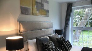 A bedroom with a large bed, a headboard, a bedside lamp, and a window with curtains. - Stunning 3 bed Lodge on Private Estate (Brentwood)