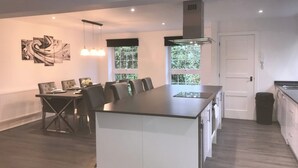 A modern kitchen with a central island, a dining area with a table and chairs, and a view of greenery through the windows. - Stunning 3 bed Lodge on Private Estate (Brentwood)