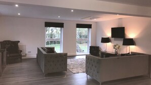 A spacious living room with a large window, a fireplace, and a flat-screen TV mounted on the wall. - Stunning 3 bed Lodge on Private Estate (Brentwood)