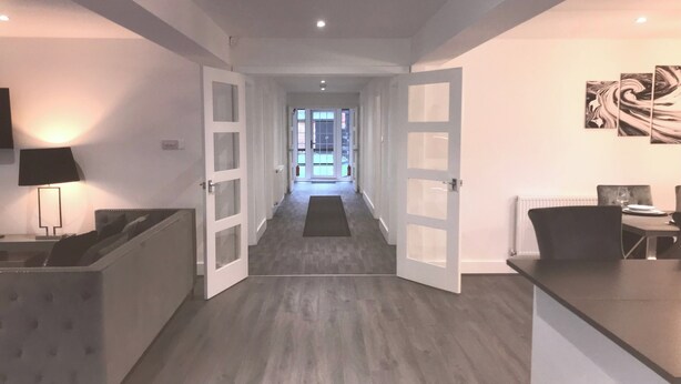 A modern kitchen with a dining area, a hallway leading to a balcony, and a TV mounted on the wall. - Stunning 3 bed Lodge on Private Estate (Brentwood)