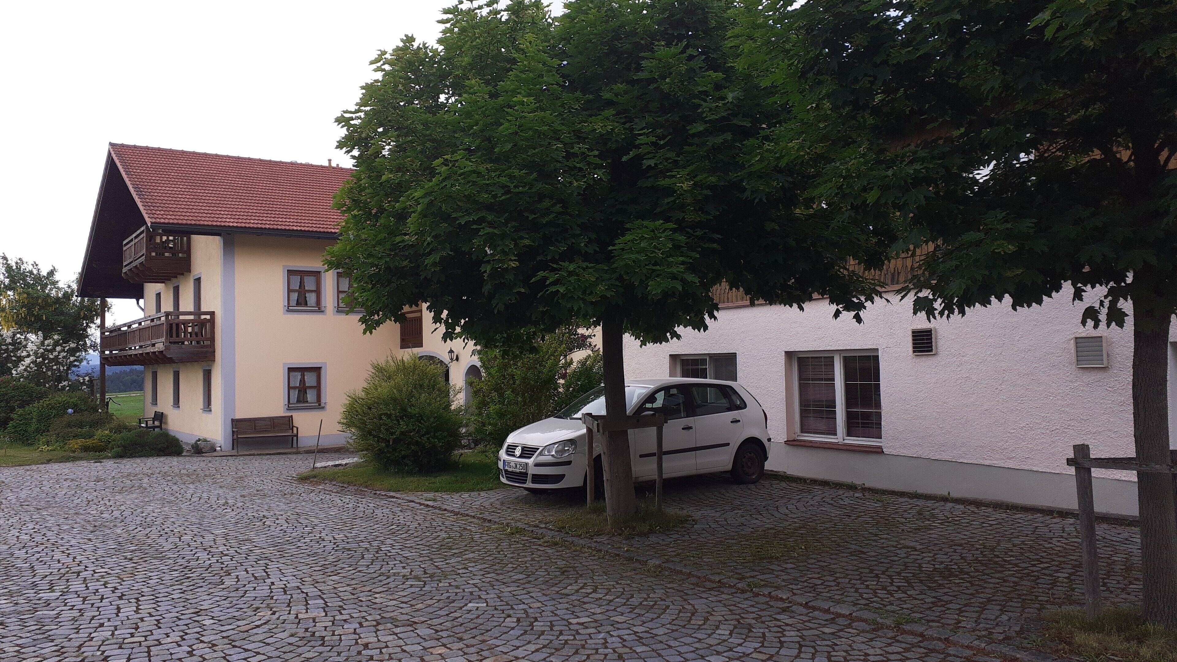 A two-story building with a red-tiled roof, a car parked in front, and a cobblestone driveway.