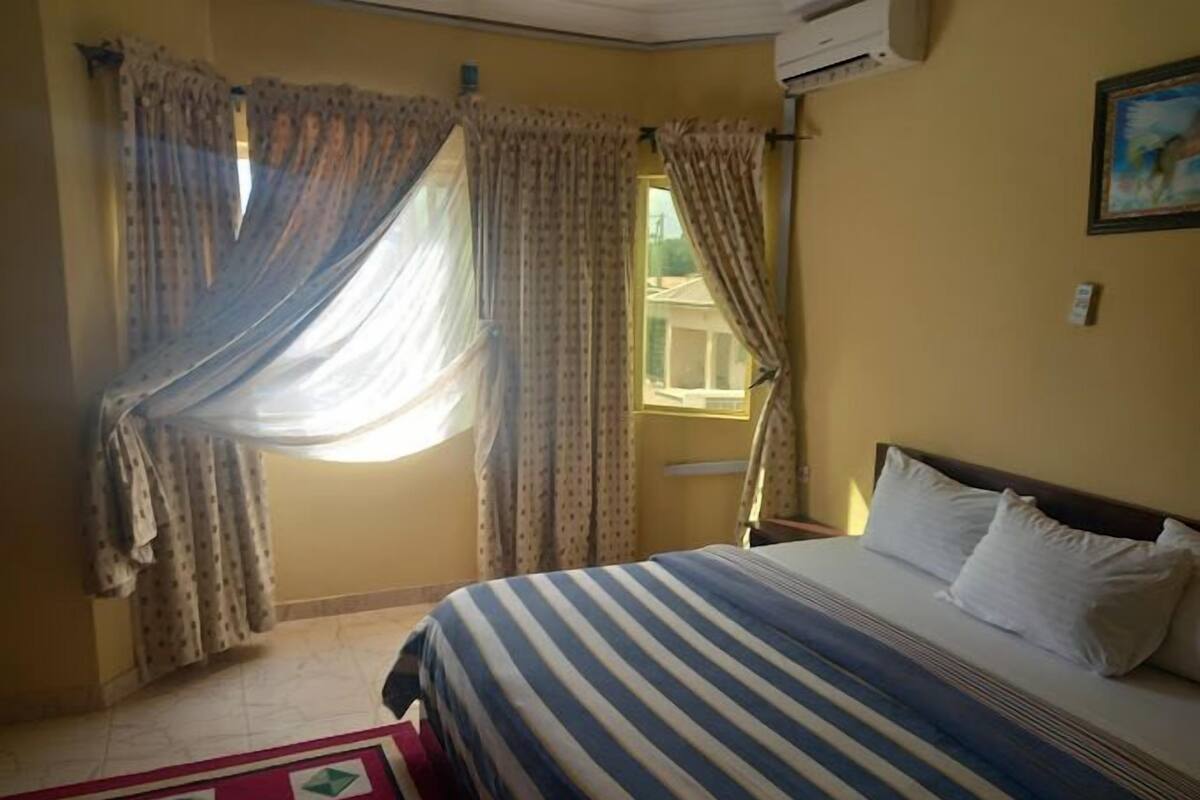 A bedroom with a bed, curtains, a window, and an air conditioning unit.