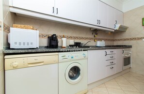A kitchen with white cabinets, a washing machine, a coffee maker, and a microwave. - Apartment Céu by D'alma Portuguesa (Silves)