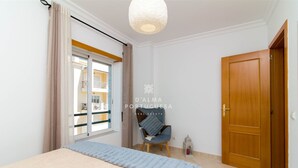 Un dormitorio con una cama, una silla, una puerta de madera y un ventanal con cortinas.