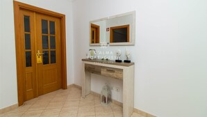 Un pasillo con puerta de madera, un espejo, una consola decorada y un pequeño farol.