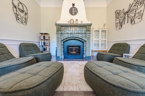Een kamer met een open haard, twee groene banken, een boekenkast en decoratieve wandkunst.