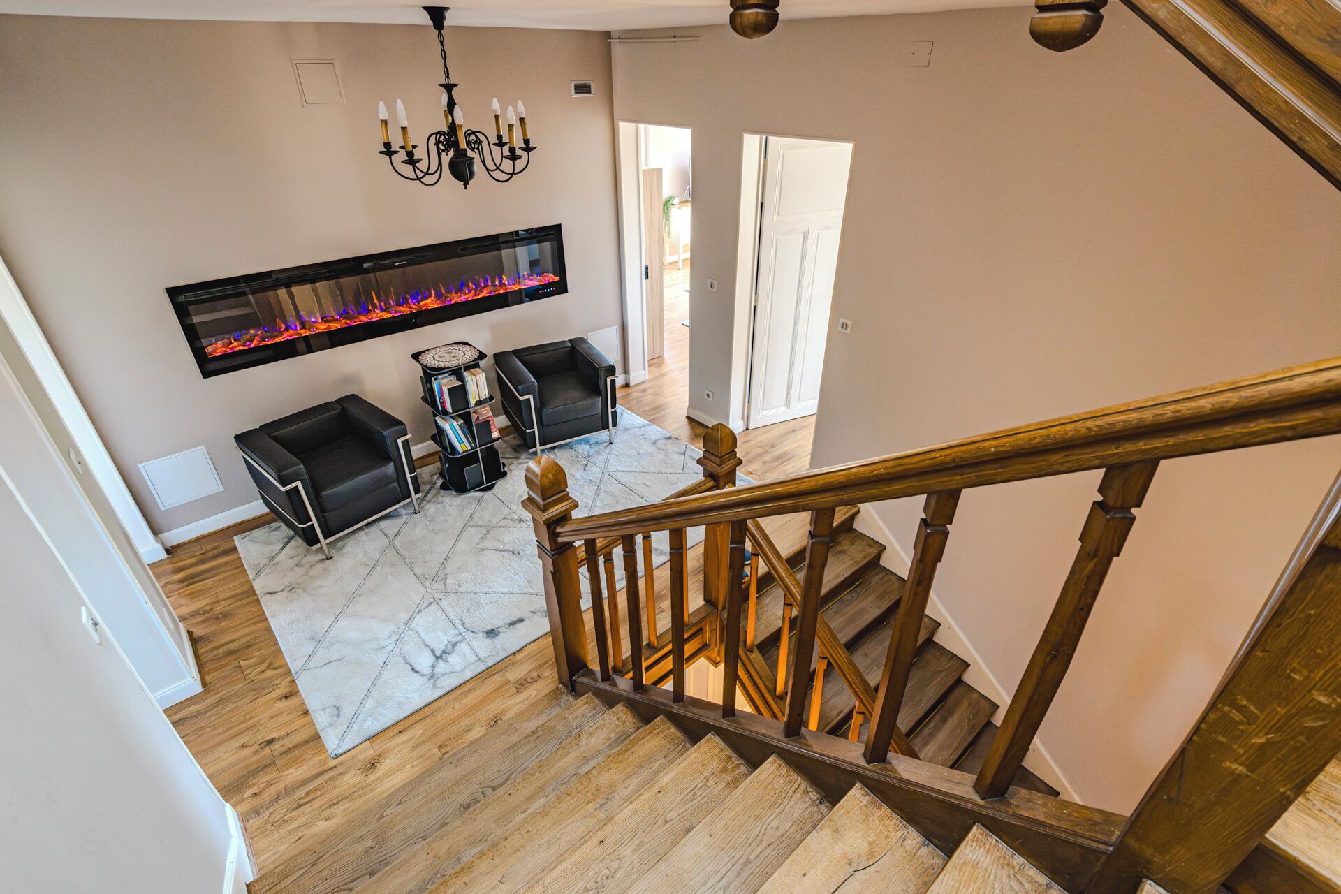 A staircase leading to a living area with a fireplace, two black sofas, and a bookshelf.