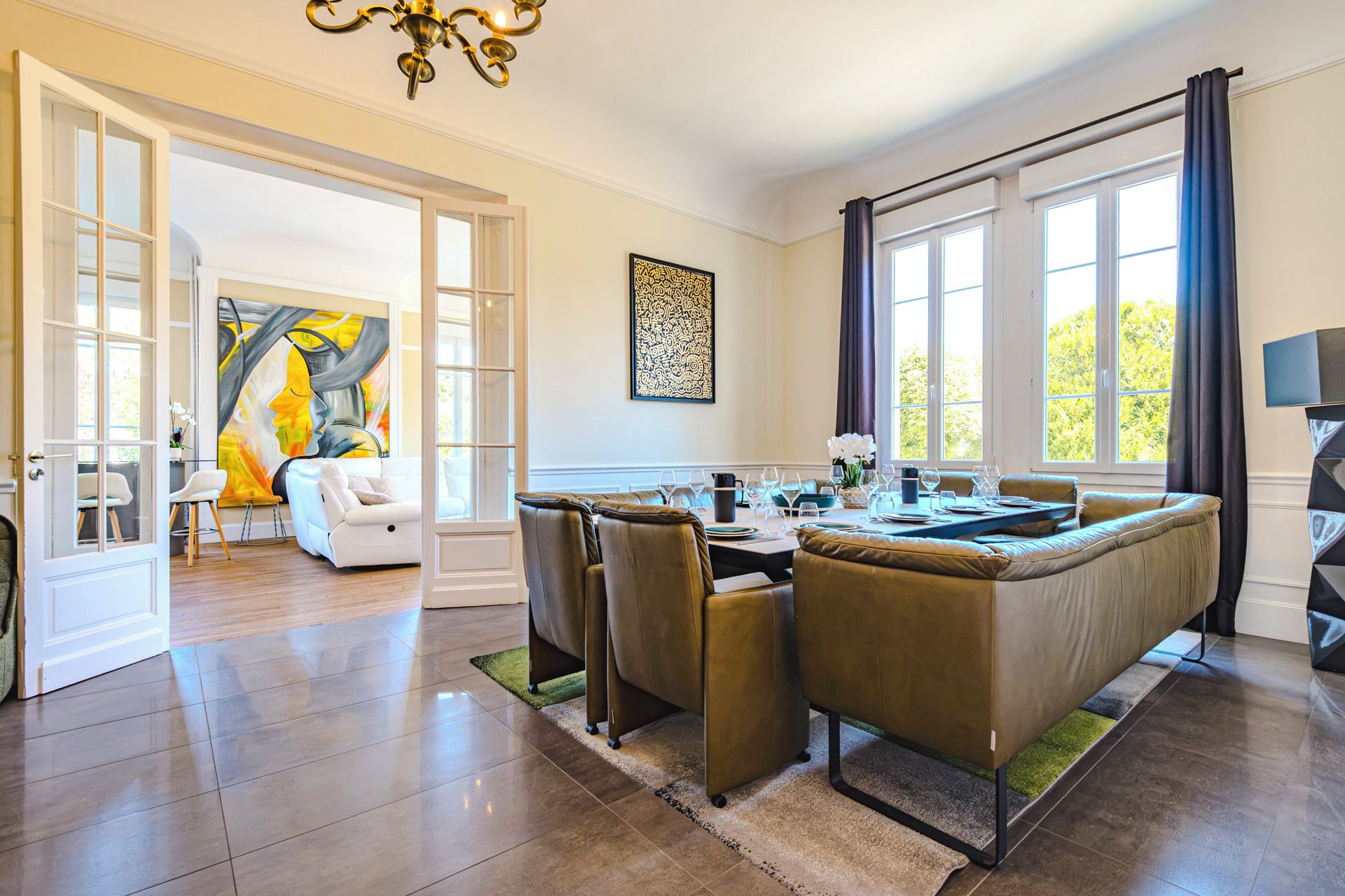 A dining area with a sofa set, a dining table set for four, and a large window with curtains.