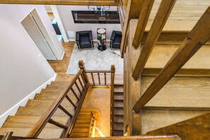 Un escalier en bois mène à une pièce comprenant un coin repas, une cheminée et une vue sur l’extérieur.