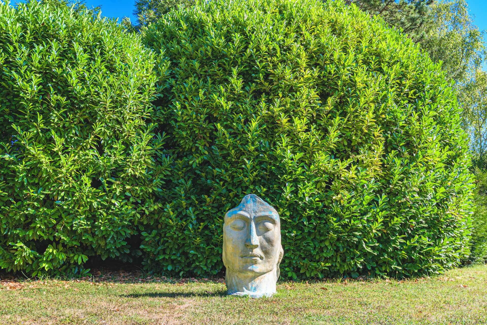 A stone sculpture in a grassy area with a dense green hedge in the background.
