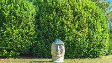 A stone sculpture in a grassy area with a dense green hedge in the background.