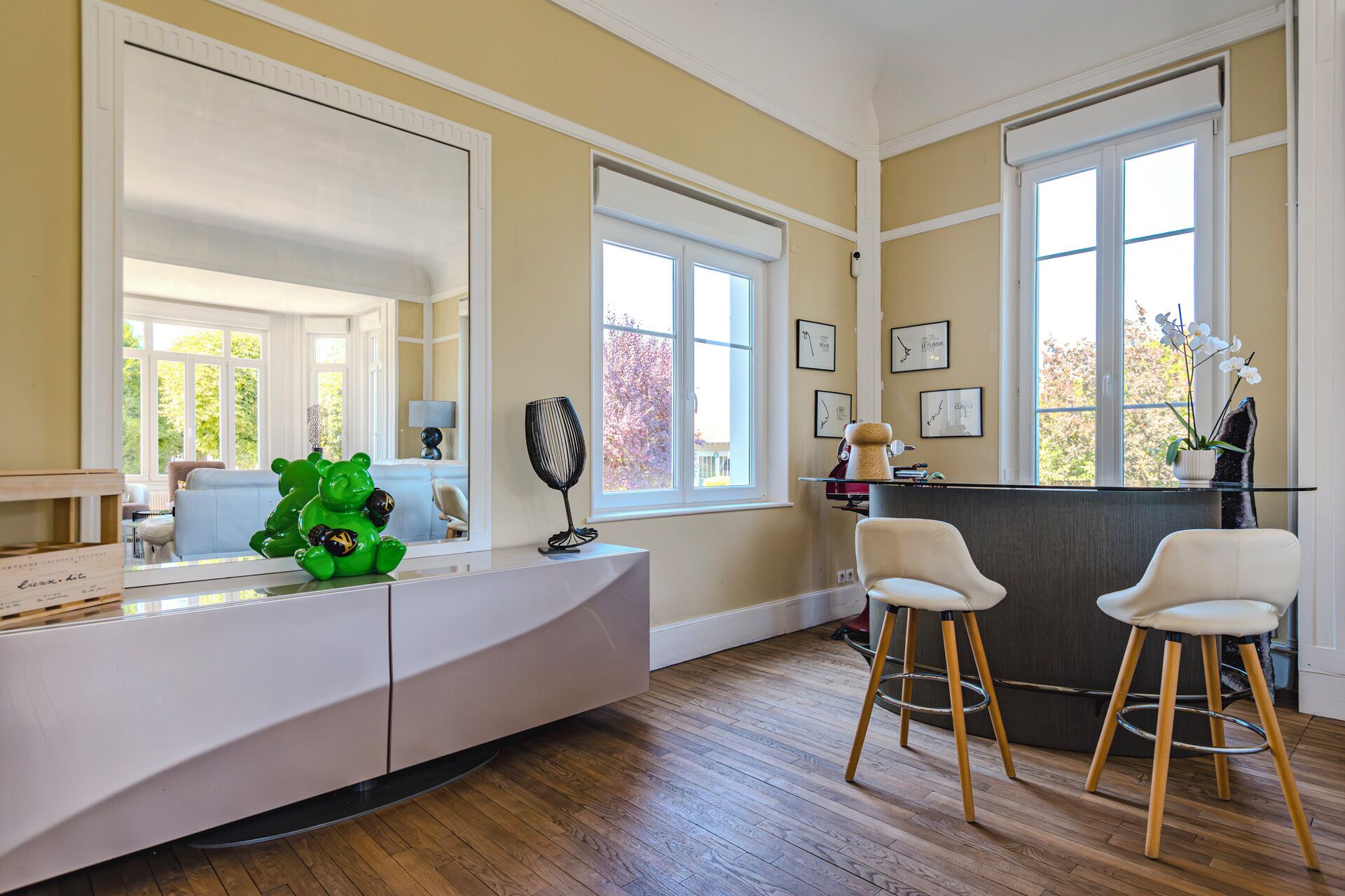A modern kitchen with a white countertop, two bar stools, and a large window.