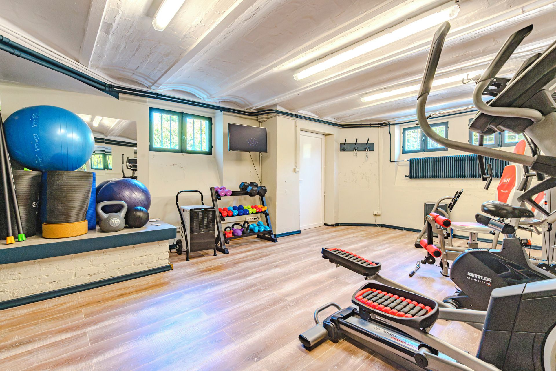 Ein Fitnessraum mit Trainingsgeräten, einem Fernseher und einem Fenster mit Jalousien.