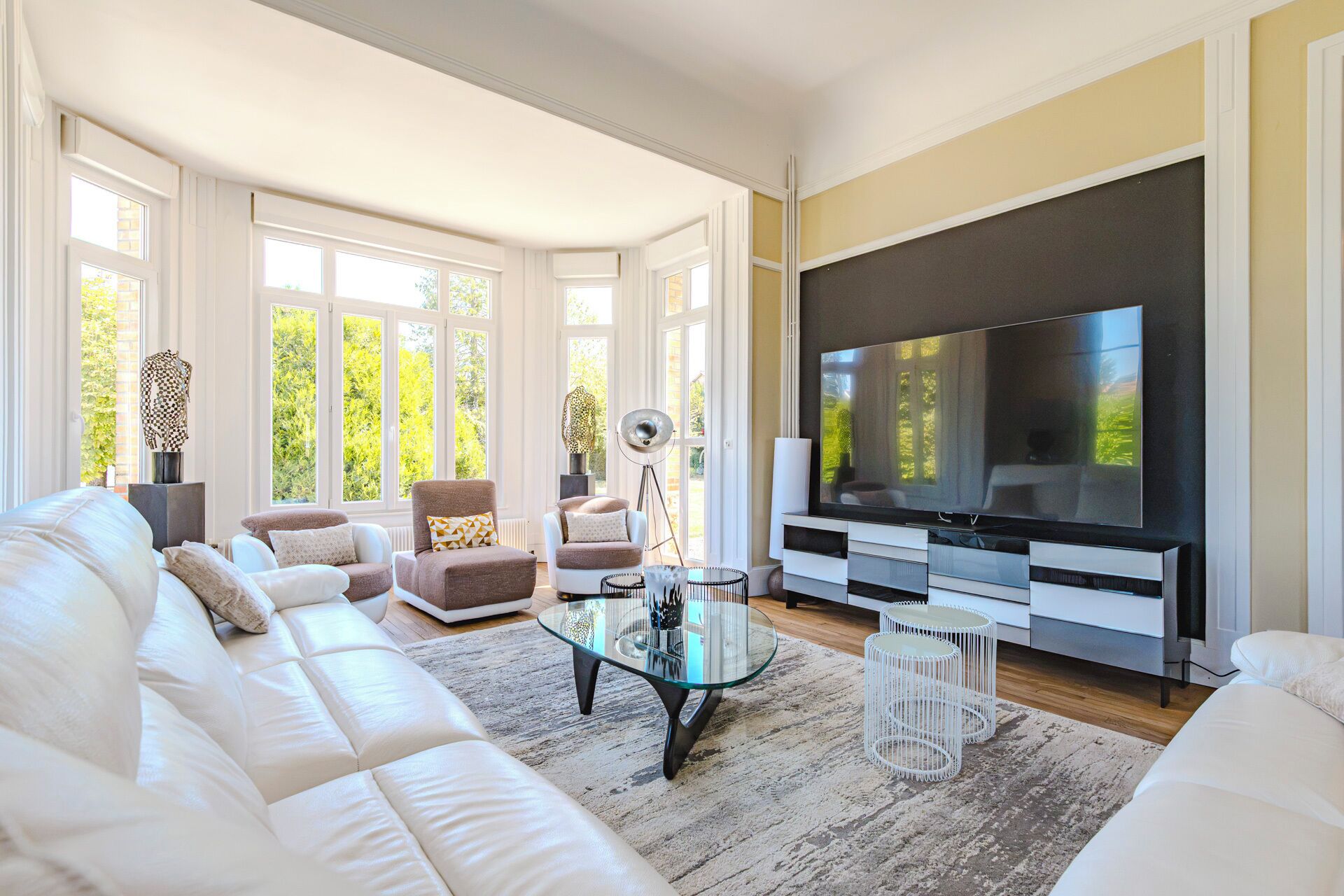 A modern living room with a large flat-screen TV, white sofas, and a glass coffee table.