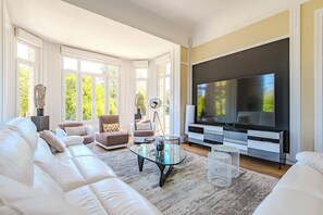 Een moderne woonkamer met een grote flatscreen televisie, witte banken en een glazen salontafel.
