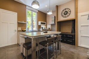 Een moderne keuken met een centraal eiland, barstoelen, een open haard van baksteen en een grote wandklok.
