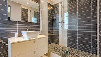 Een moderne badkamer met een wit badkamermeubel, een douchecabine met glazen wanden en donkere betegelde muren.